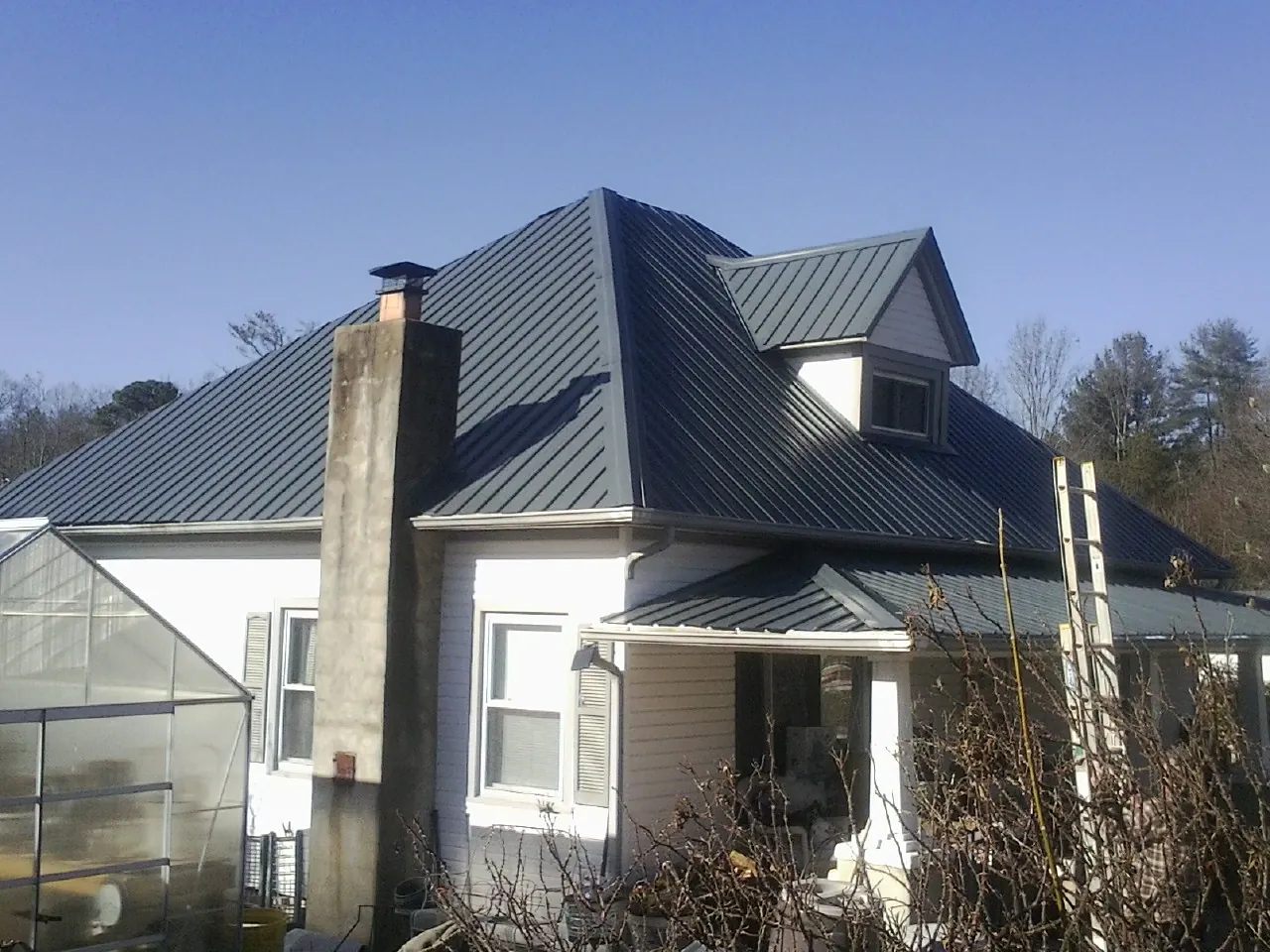 Dark blue standing seam metal roof on a white farmhouse with dormer — Slate & Tile Roof Repair by Roofing Brothers in Donnellson