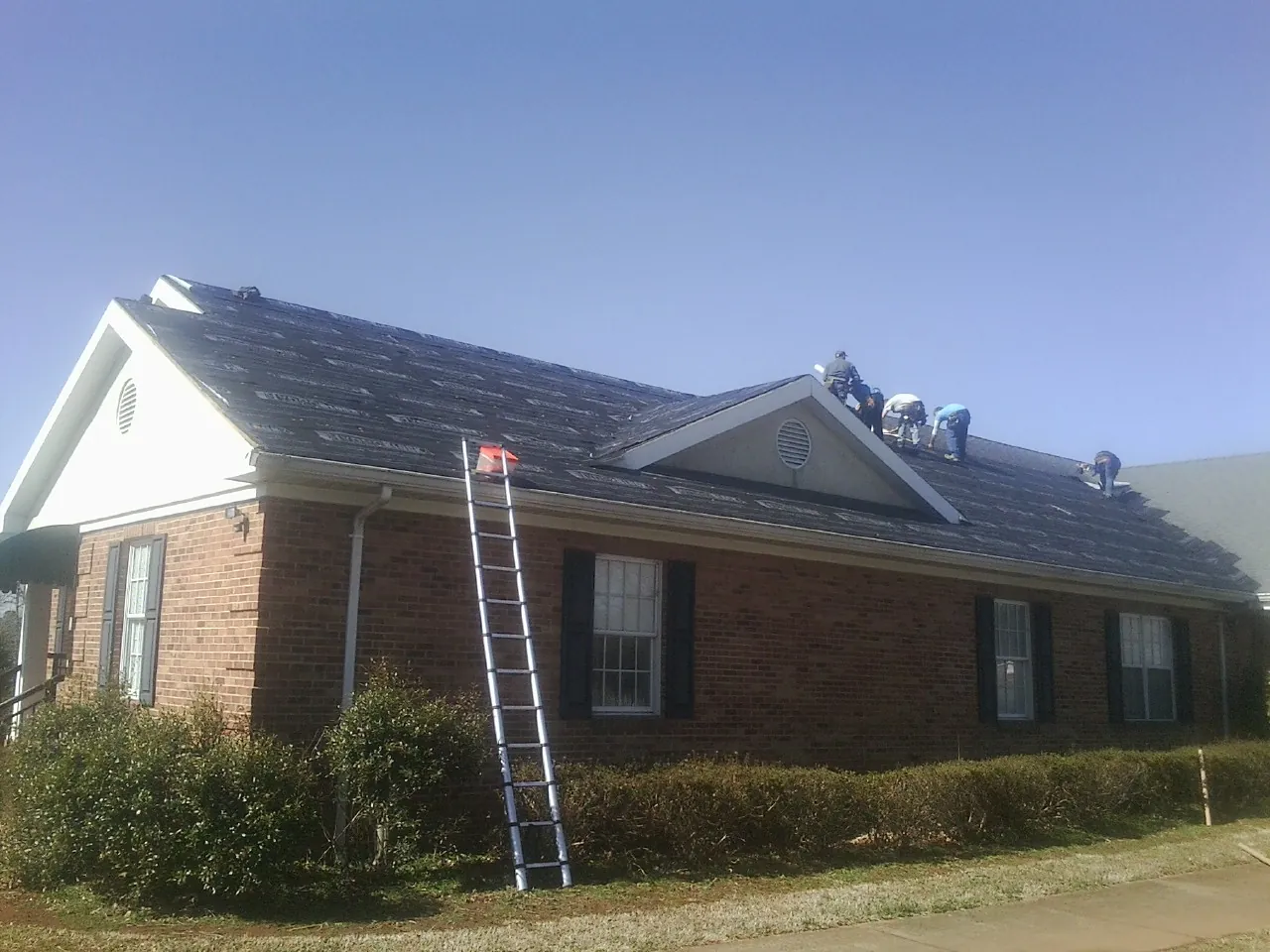 Crew tearing shingles off a brick ranch roof with a ladder set — Emergency Roof Repair work by our crew in Donnellson