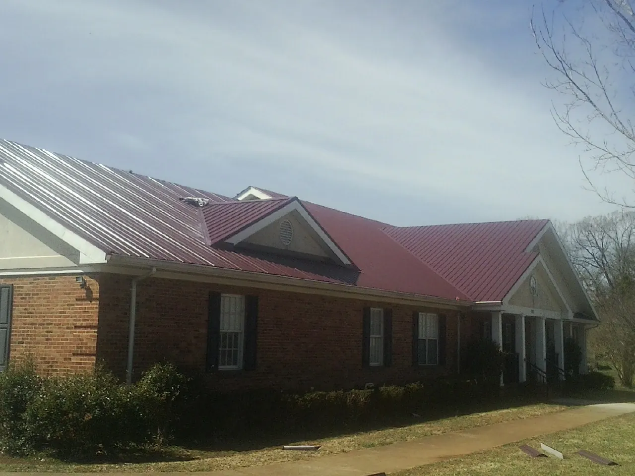 Red metal roof with gabled entries on a long brick building, from a Hail Damage Roof Repair job in Donnellson