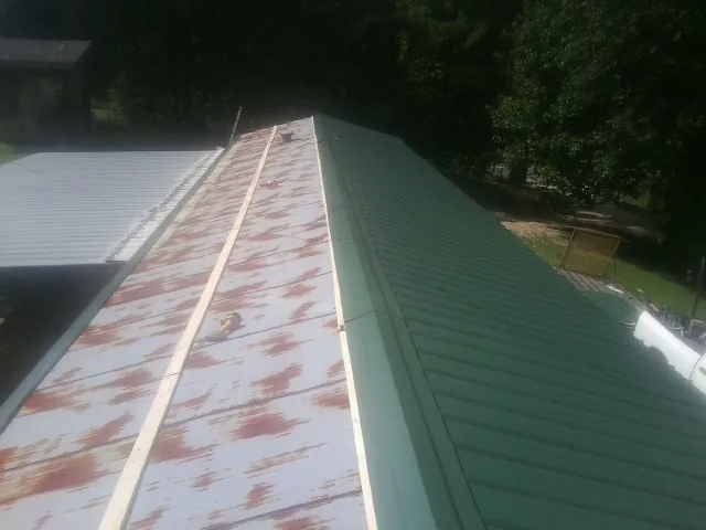 Old rusted panels beside newly installed green metal roofing — Wind Damage Roof Repair by Roofing Brothers in Donnellson