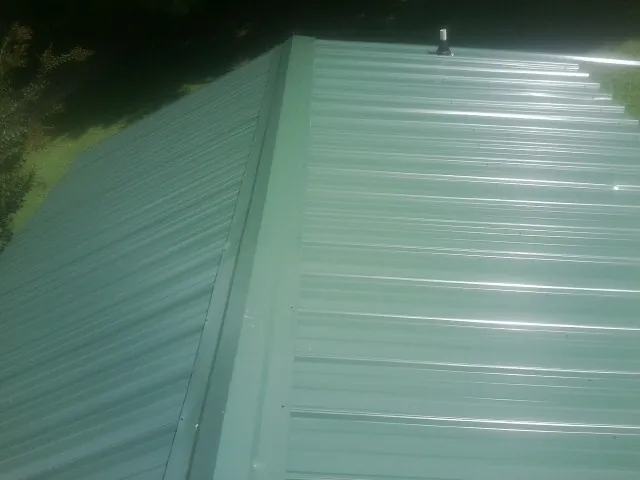 New green metal panels meeting at the ridge of a roof — Flat Roof Repair work by our crew in Donnellson