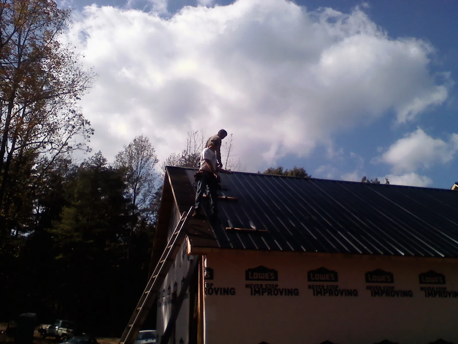 Roofer fastening dark metal panels high against a cloudy sky, from a Roof Inspection job in Donnellson