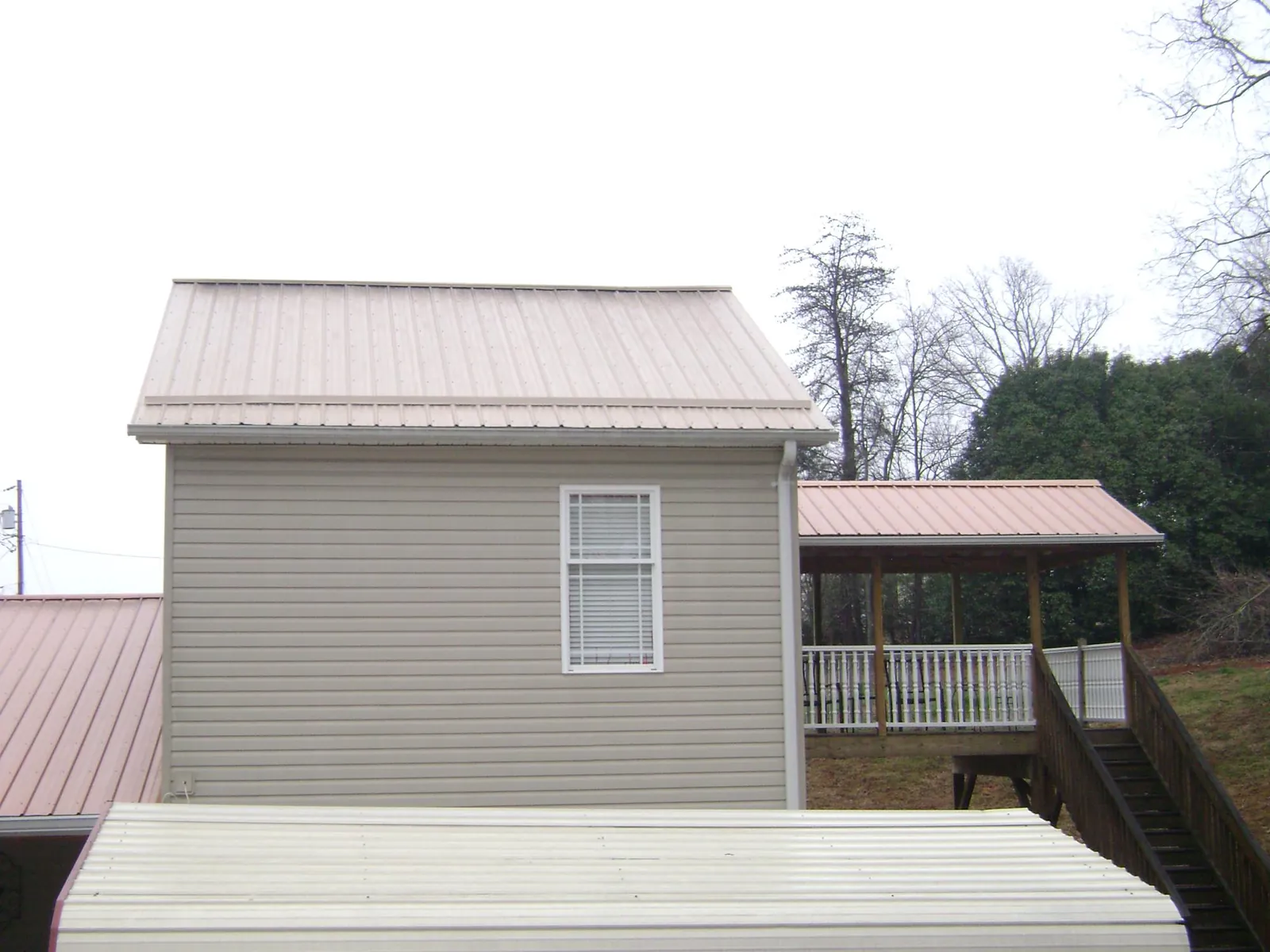 Tan metal roofs on a two story addition and attached porch, from a Roof Replacement job in Donnellson